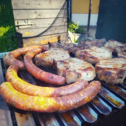 Featured image for "BBQ – A South-East European Specialty" article on Zacks.eu, representing a screenshot of a various meat cuts placed on a BBQ grate.