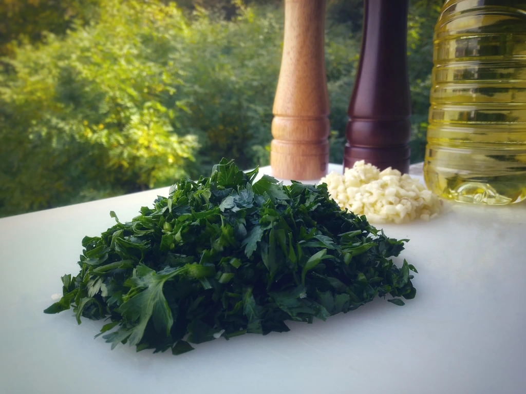 Fresh parsley and chopped garlic with oil, salt and pepper in the background.